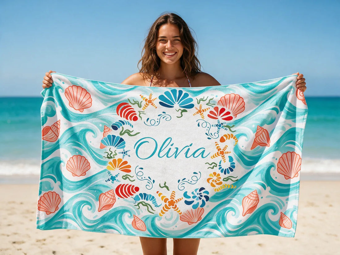 Woman on a sunny beach holding up a personalized beach towel with the name Olivia in a seashell wreath